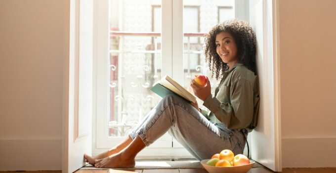 Happy Black Woman Reading Book At Home Relaxing On Floor