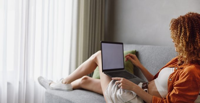 Young woman with curly hair using laptop on a cozy sofa, showcasing a relaxed lifestyle and modern