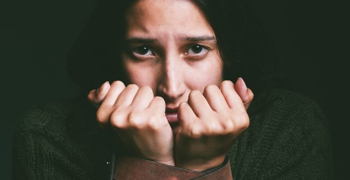 Shot of a young woman looking scared with a belt tied around her arms against a black background