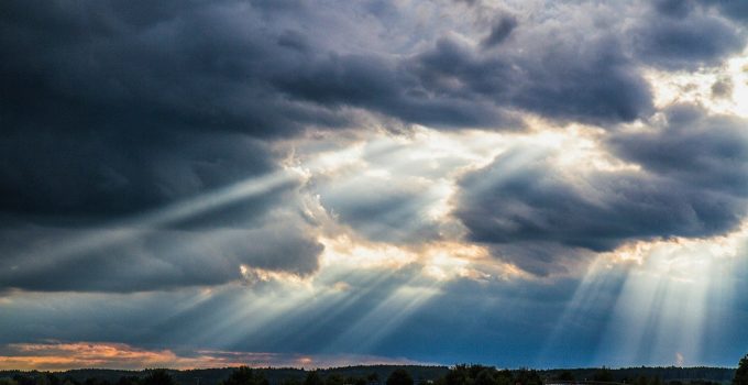 Sunlight streaming through dark storm clouds over a rural road and field