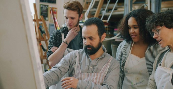 A group of four coworkers in aprons gathered together in a studio workshop, discussing a project